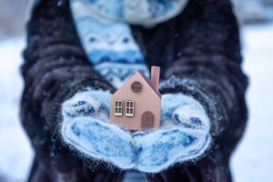 Frau hält kleines Haus mit Schal in der Hand