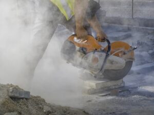Ein Arbeiter schneidet eine Fliese mit einer elektrischen Schleifmaschine unter starker Rauchentwicklung zurecht. Konzept der Umweltverschmutzung